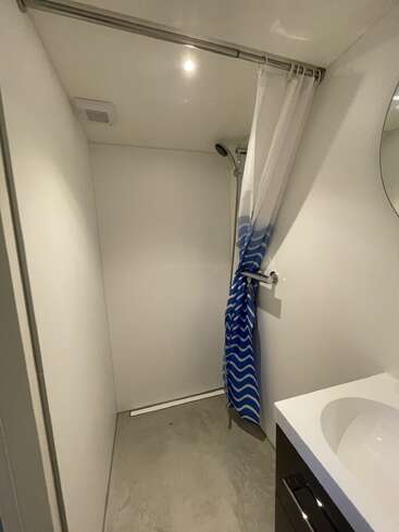 Dieses Bild zeigt ein minimalistisches Badezimmer mit einer begehbaren Dusche, einem blau-weißen Chevron-Duschvorhang, einem einfachen Waschbecken, einem Spiegel und einem Betonboden.