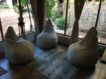 La imagen muestra una acogedora habitación con tres pufs, una alfombra y una ventana con vistas a un jardín, que desprende un ambiente cálido y acogedor.