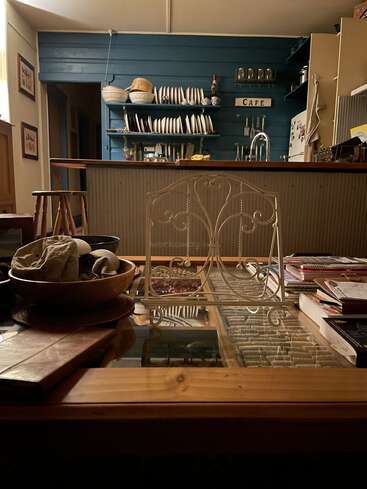 Eine gemütliche, rustikale Küche mit blauen Wänden, offenen Regalen mit Geschirr, einem hölzernen Tresen, Büchern und Schalen auf einem gläsernen Couchtisch, warme, einladende Atmosphäre.