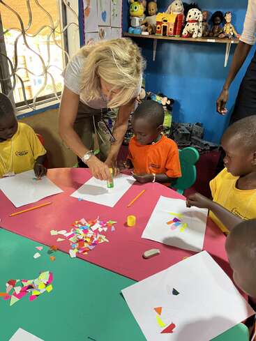 Une enseignante aide de jeunes enfants à réaliser un projet d'artisanat en papier coloré dans une salle de classe remplie de jouets, de dessins et d'une créativité vibrante, encourageant l'apprentissage collaboratif et l'amusement.