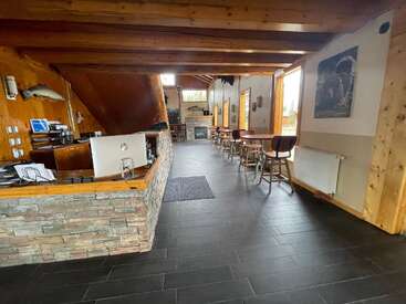 Ce hall d'accueil confortable comprend un comptoir d'accueil en pierre, des poutres apparentes, un sol carrelé, plusieurs petites tables et chaises, de grandes fenêtres, des décorations animalières et une cheminée à l'arrière.