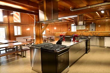 Cette image montre une cuisine spacieuse et moderne avec des murs et des plafonds en bois, des appareils électroménagers en acier inoxydable, de grands espaces de travail, des bancs pour manger et un éclairage naturel abondant. Atmosphère chaleureuse et accueillante.