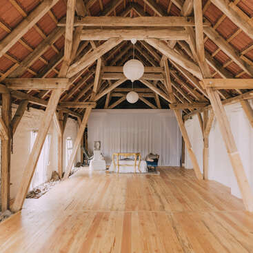 Das Bild zeigt das Innere eines geräumigen Zimmers mit Holzboden und -decke, mit einem weißen Vorhang, Möbeln und dekorativen Elementen, die ein Gefühl von Eleganz und Raffinesse ausstrahlen.