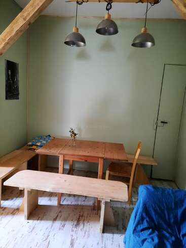 A cozy room featuring a wooden table, benches, and chair. Three pendant lights hang above. There’s a blue armchair and a small wall picture.