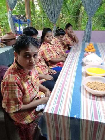 L'image représente un groupe d'enfants assis à une longue table, portant des chemises à carreaux assorties, avec une nappe rayée et divers bols de nourriture devant eux.