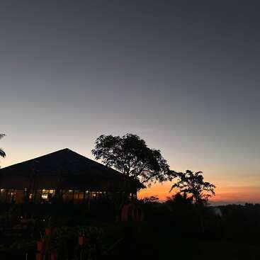 A peaceful sunset scene features a silhouetted house, two trees, and a glowing orange sky fading into night, creating a tranquil and serene evening atmosphere.