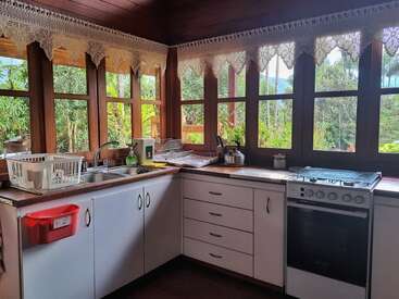 L'image représente une cuisine avec des armoires blanches, un évier en acier inoxydable et une cuisinière, avec une fenêtre offrant une vue sur des arbres et une clôture à l'arrière-plan.