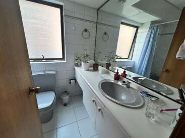 This is a tidy bathroom with two sinks, a mirror, plants, hygiene products, toothbrushes, a glass, toilet, two windows, tiled walls, and floor.