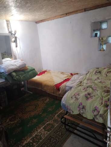 Esta acogedora habitación tiene dos camas individuales, una alfombra verde estampada, paredes blancas, una pequeña ventana, algo de ropa de cama, un espejo y un trofeo expuesto.