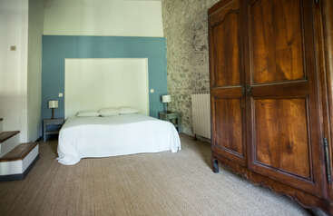 Este acogedor dormitorio cuenta con un gran armario de madera, una cama doble con ropa de cama blanca, mesillas de noche y lámparas, una pared de acento azul y una pared con textura de piedra.