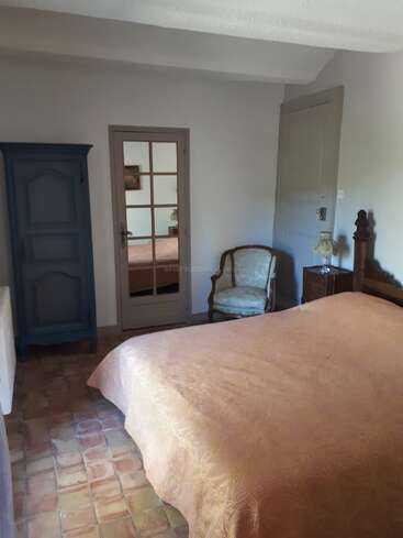 Un dormitorio acogedor con una cama grande cubierta con una colcha melocotón, un armario azul, un sillón, suelo de baldosas y una puerta con paneles de cristal.