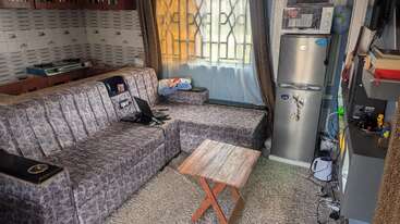 A aconchegante sala de estar tem um sofá estampado, mesa de centro de madeira, geladeira, micro-ondas, TV, estantes e cortinas estampadas com luz natural que entra pela janela.