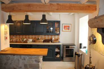 Cette cuisine accueillante présente des armoires sombres, un comptoir en bois, des lampes suspendues, un dosseret en carrelage, des poutres apparentes, des étagères ouvertes, un four en acier inoxydable et des accents en pierre, créant ainsi une ambiance rustique.