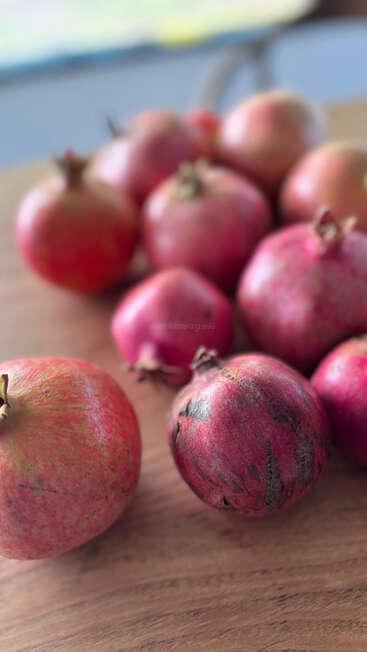 Mehrere frische, reife Granatäpfel liegen auf einer Holzfläche. Der Fokus liegt auf der vorderen Frucht, während der Hintergrund schön unscharf bleibt und ihre leuchtend rote Farbe hervorhebt.