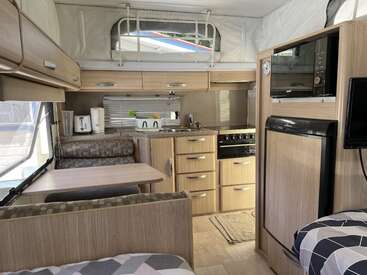 This image shows the cozy interior of a modern camper van, featuring a kitchen, dining area, appliances, compact fridge, storage cabinets, and a bed.