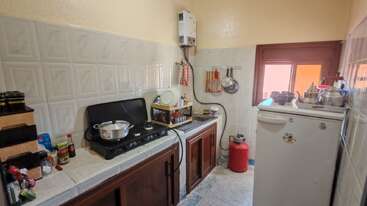 Cette cuisine compacte est équipée d'une cuisinière à gaz, de murs en carrelage blanc, d'armoires en bois foncé, d'un réfrigérateur de comptoir, d'ustensiles, de couverts et d'ustensiles de cuisine, et d'une fenêtre apportant de la lumière naturelle.