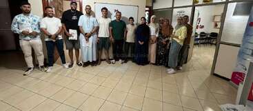 Un groupe de treize personnes se tient en souriant dans une pièce bien éclairée avec "ELC" sur le mur, suggérant un rassemblement formel ou un événement éducatif dans un centre d'apprentissage.