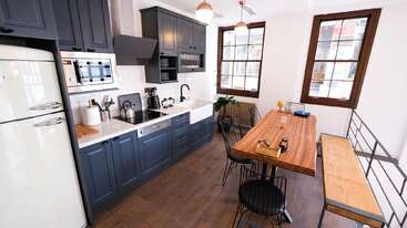 The image depicts a modern kitchen with a large island, featuring a sink and stove, accompanied by a dining table and chairs, and a living room area with a couch and coffee table.