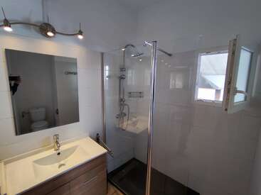 This modern bathroom features a glass shower enclosure, small window, wall-mounted sink, rectangular mirror, toilet, and overhead lighting, all in a clean, minimalist design.