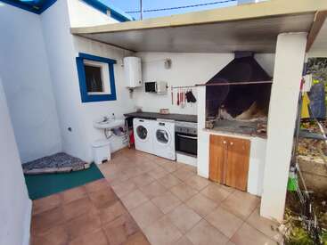 This image shows an outdoor utility area with a washing machine, dryer, sink, oven, barbecue grill, microwave, and storage cabinets, under a partial roof.