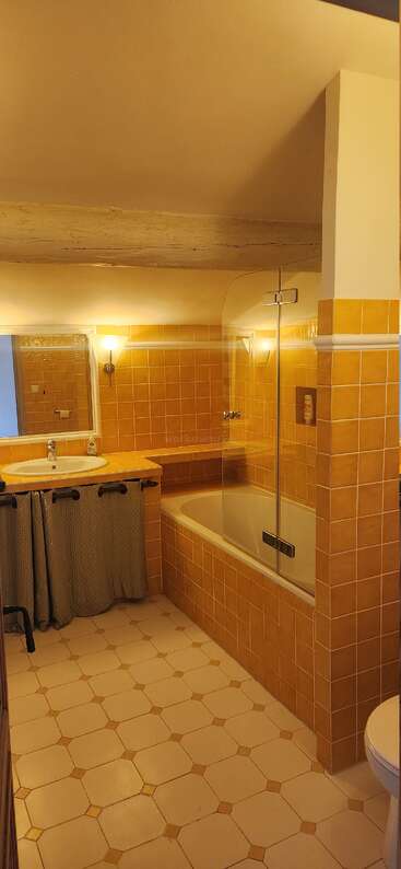 La imagen muestra un cuarto de baño con lavabo blanco, bañera e inodoro, en el que predomina el blanco con toques grises y marrones. Las paredes están adornadas con un motivo decorativo.