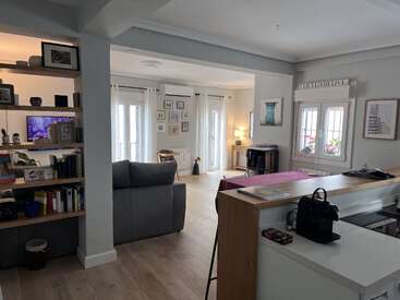 A imagem mostra uma sala de estar moderna e aberta com cozinha, sala de jantar e sala de estar, com paredes brancas e piso de madeira.