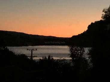 The image depicts a serene lake scene at sunset, featuring a telephone pole and trees in the foreground, with hills and a vibrant orange sky in the background.