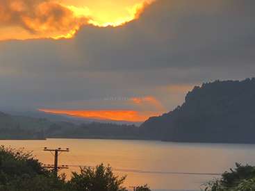The image depicts a serene lake scene at sunset, with a telephone pole and trees in the foreground, set against a backdrop of hills and a cloudy sky.