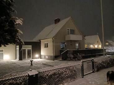 L'image représente une scène hivernale sereine d'une maison de nuit, avec un sol enneigé et une cour clôturée, évoquant une atmosphère paisible et tranquille.