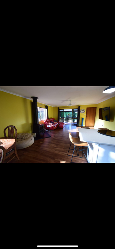 This room features yellow walls, wood flooring, a wood fireplace, red couches, a beanbag, a dining table, a breakfast bar, TV, and large windows.