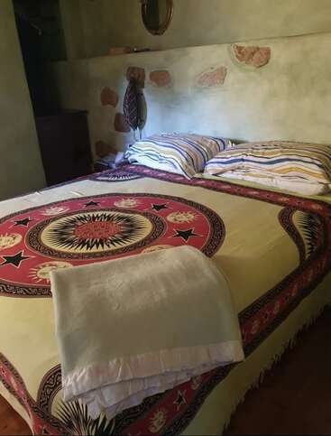 Ein gemütliches Schlafzimmer mit einem Bett, das mit einer leuchtenden Decke mit Sonnen- und Sternenmustern bedeckt ist, gestreiften Kissen, einer rustikalen Steinwand, einem Spiegel und sanfter Umgebungsbeleuchtung.