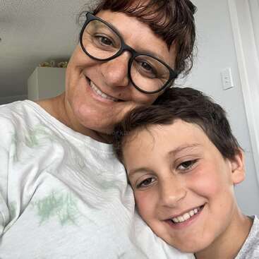 L'image montre une femme et un garçon posant pour un selfie, la tête de la femme reposant sur l'épaule du garçon, tous deux souriant à l'appareil photo.