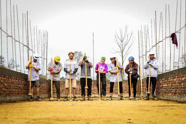 Das Bild zeigt eine Gruppe von Menschen, die zusammenarbeiten, wahrscheinlich auf einer Baustelle, mit einer Mischung aus Werkzeugen und Materialien, die ein Gefühl von Teamwork und Zusammenarbeit vermitteln.
