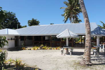 The image depicts a tropical setting with a building featuring a pitched roof, surrounded by palm trees and a body of water, evoking a sense of relaxation and tranquility.