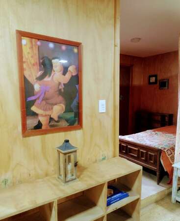 The image shows a cozy room with wooden walls, a framed painting of a dancing couple, a decorative lantern, bookshelf, and a quilt-covered bed visible through a doorway.