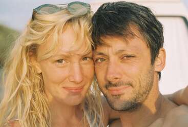 Ein lächelndes Paar macht draußen im Sonnenlicht ein Selfie in Nahaufnahme. Die Frau trägt eine Sonnenbrille auf dem Kopf. Beide sehen glücklich und entspannt aus und genießen ihre gemeinsame Zeit.