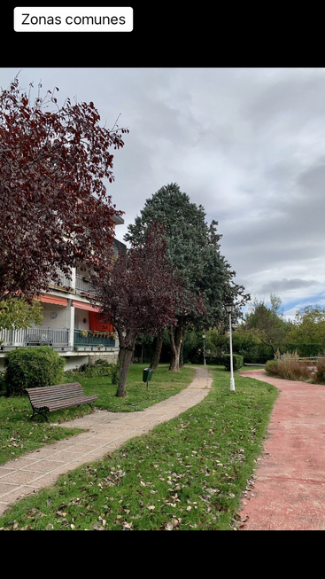 The image depicts a serene residential area with a paved path, benches, trees, and a building, set against an overcast sky.