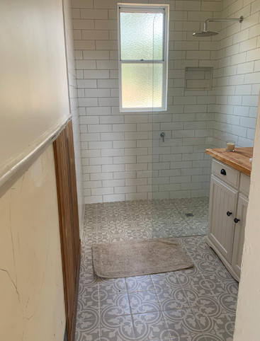 Cette image montre une petite salle de bains avec des carreaux de sol à motifs, des murs blancs en carreaux de métro, une douche à l'italienne, une fenêtre, un meuble-lavabo et un tapis beige.