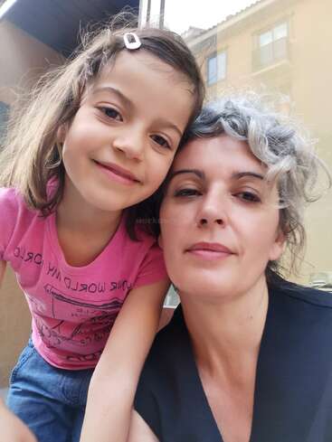 A imagem mostra uma mulher e uma menina posando para uma selfie, com a mulher à direita e a menina à esquerda, ambas olhando para a câmera.