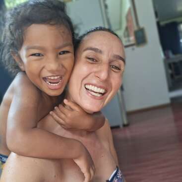 A joyful moment is captured as a child playfully hugs an adult from behind. Both are smiling widely, radiating happiness and warmth in a home setting.