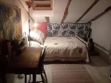 Dieses gemütliche Schlafzimmer im Dachgeschoss hat eine schräge Decke, ein Einzelbett mit gemusterten Stoffen, einen Schreibtisch mit einer Nähmaschine, warme Beleuchtung und künstlerische Dekorationen.