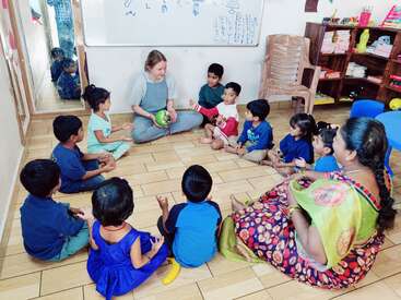 Eine Gruppe kleiner Kinder sitzt im Kreis um zwei Lehrer/innen in einem Klassenzimmer und nimmt eifrig an einer lustigen und interaktiven Lernaktivität teil.