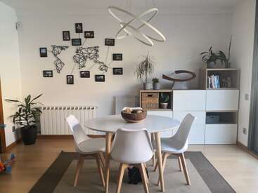 The image depicts a modern dining room with a white table and chairs, a geometric light fixture, and a wall featuring a world map and various decorative items.
