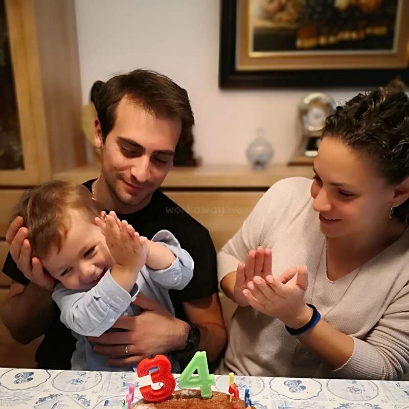 The image shows a family of three celebrating a birthday, with a cake featuring candles displaying the numbers 3 and 4, likely marking a child\'s third or fourth birthday.