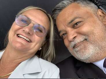 Una mujer sonriente con gafas y pelo rubio se toma un selfie de cerca con un hombre sonriente de pelo y barba canosos, ambos aparecen juntos felices y alegres.