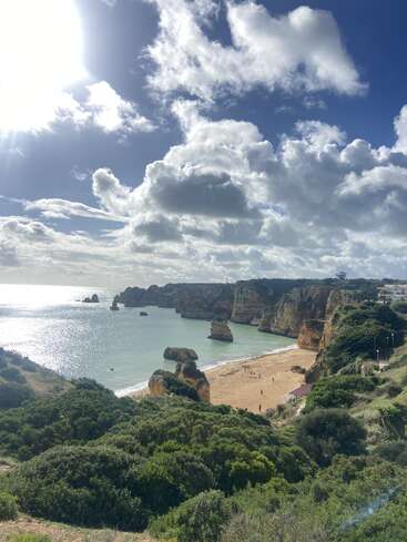 Un magnifique paysage côtier avec des falaises spectaculaires, une plage de sable doré, des rochers éparpillés dans la mer, une végétation luxuriante et un ciel parsemé de nuages lumineux.