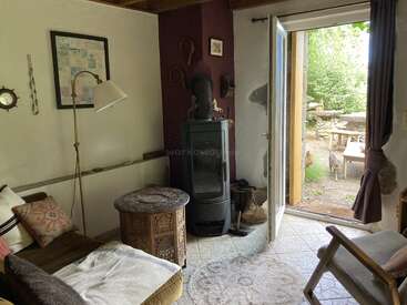 Salon confortable avec une décoration éclectique, un poêle à bois, des coussins à motifs et des œuvres d'art uniques. La porte s'ouvre sur un patio paisible avec des sièges extérieurs et de la verdure.