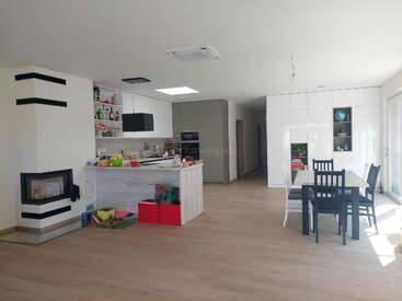 Dieses Bild zeigt einen modernen, offenen Küchen- und Essbereich mit minimalistischen Möbeln, heller Beleuchtung, Holzböden, einem Kamin und verstreutem Kinderspielzeug in der Nähe der Insel.