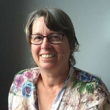 The image features a woman with short, gray hair and glasses, wearing a floral top, set against a gray background with a subtle watermark reading \"workaway.info\".