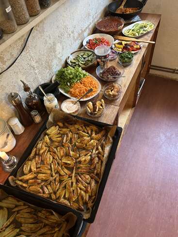 A delicious homemade buffet featuring baked potato wedges, fresh vegetables, assorted sauces, beans, and toppings neatly arranged on a rustic wooden table for self-service.